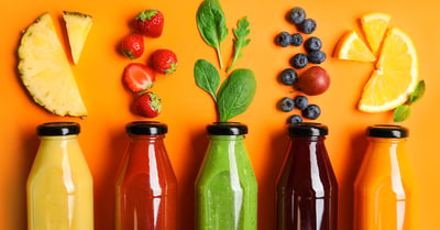 Bottles with delicious juices and fresh ingredients on orange background